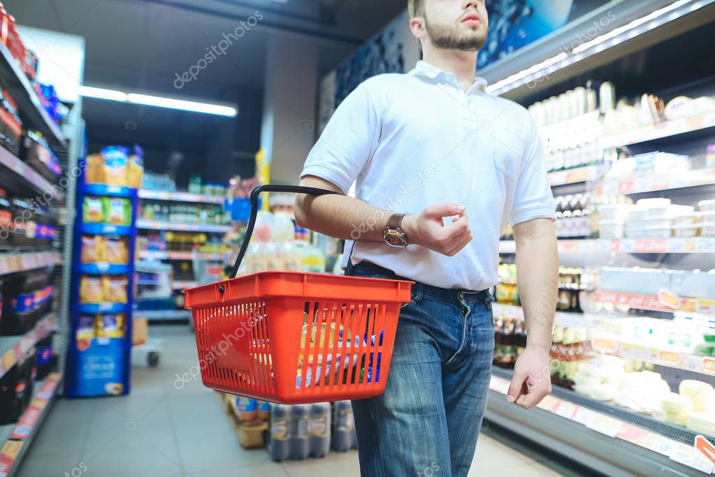 A man with a red shopping basket strolls around the supermarket. A man buys goods in a supermarket.