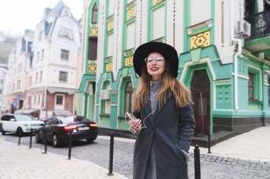 Güzel mimari arka plan üzerinde koyar ve müzik dinleyen bir şık olumlu kız portresi. Güzel bir kadın caddenin tarihi kentin arka plan üzerinde durumda.