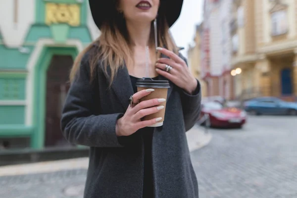 En stilfuld kvinde holder en kop kaffe eller te i hænderne. Varm drink i hænderne på en smuk kvinde. Hænder close-up og i fokus . - Stock-foto