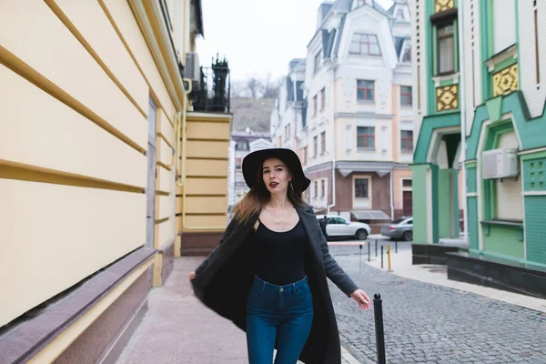 Eine stylische schöne Frau posiert vor der Kulisse einer schönen Altstadtstraße für die Kamera. das Mädchen dreht sich auf der Straße vor der Kamera. — Stockfoto