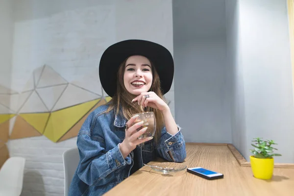 Portræt af en sjov hipsters pige med en kop kaffe i hånden. En smilende pige fra en cafe ser på kameraet og smiler . - Stock-foto