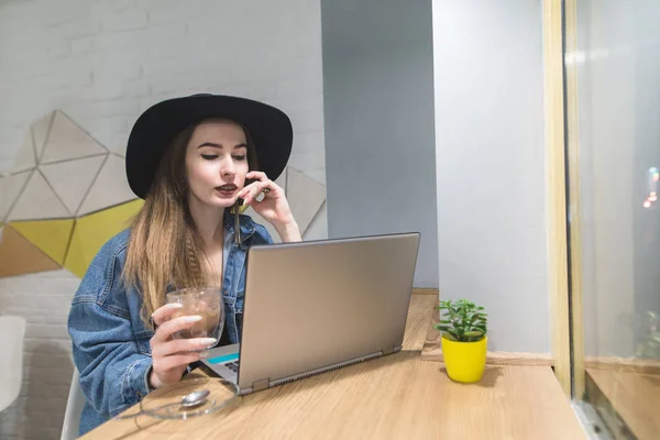 Стильна дівчина працює на ноутбук у затишному кафе з чашкою гарячого напою. Портрет вільного хіпстера кафе . — стокове фото