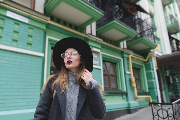 Portræt af en stilfuld kvinde i briller og hatte på baggrund af arkitekturen i den gamle bydel. En smuk pige udgør på baggrund af gammel arkitektur . - Stock-foto