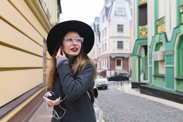 En stilfuld kvinde korrigerer hovedtelefoner i ørerne på baggrund af gammel arkitektur. En turist pige slentre ned ad gaderne i byen og lytter til musik i hovedtelefonerne . - Stock-foto
