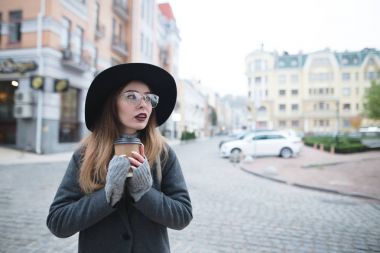 Onun elinde kahvesiyle şık güzel bir kadın eski şehrin manzara arka planda durumda. Bir fincan kahve şehrin arka planı ile bir kız portresi.