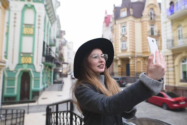 Fille touristique élégant prend selfie sur le fond d'une belle vieille ville. Les hipsters sont photographiés sur leur téléphone . — Photo