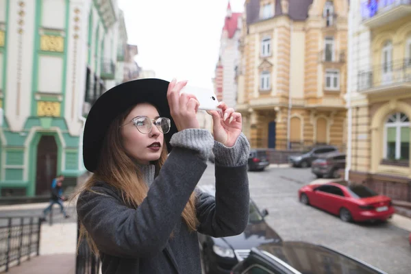 Menina turista elegante fotografa a arquitetura da cidade velha no telefone. Retrato de uma linda garota que tira uma foto móvel em um smartphone . — Fotografia de Stock