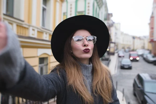 スタイリッシュな女の子は、美しい街歩きしながら通り selfie を取ります。電話と selfie のカメラにポーズ観光ヒップスター. — ストック写真