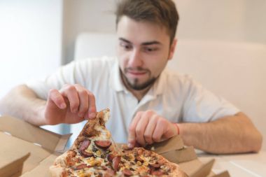 Aç bir göz ile yakışıklı bir adam bir parça pizza kutudan sıkılaştırır ve yaklaşık yemek etmektir. İştah açıcı bir sıcak pizza restoran ile öğle yemeği.