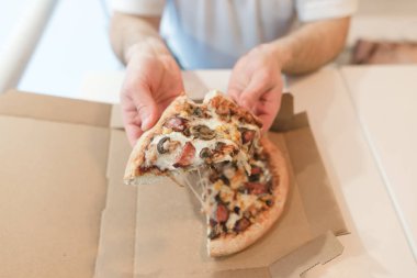 Dilim iştah açıcı pizza erkek elinde. Bir adam bir kağıt kutusundan bir sıcak pizza yiyor.