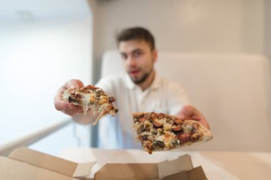 Adam iki dilim pizza elinde tutar ve fotoğraf makinesine gönderir. Bir adam bir pizza sunuyor. Bir adam elinde güzel bir pizza.