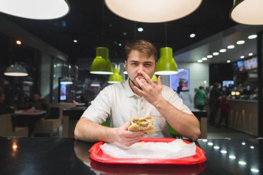 Yakışıklı bir adam bir fast food bir hamburger yiyor ve parmağını yalıyor