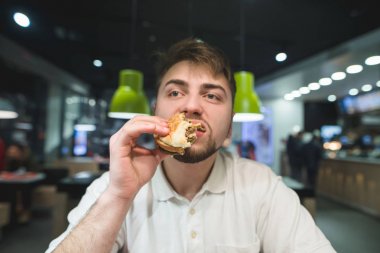 Aç bir adam bir fast food Restoran, lezzetli bir burger sahiptir. Adam hızlı yemek yiyor.