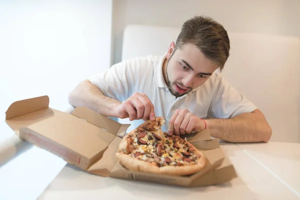 Aç yakışıklı adam bir parça taze pizza kutusundan alır. Bir sakallı bir adam pizza yemek etmektir. Hızlı öğle yemeği pizza. — Stok fotoğraf