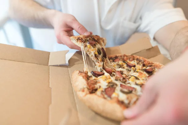 Las manos de los hombres toman un pedazo de pizza caliente. El hombre comerá deliciosa pizza con queso. Enfoque en pizza . — Foto de Stock