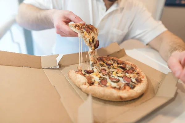 Adam bir parça sıcak pizza kutusundan alır. El ile bir parça iştah açıcı pizza. Peynir pizza eritebilir. Pizza üzerinde odaklanmak — Stok fotoğraf