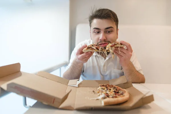 Hombre hambriento con barba comiendo pizza de una caja de cartón. Un hombre con barba tiene trozos de pizza en sus manos y se los va a comer. . — Foto de Stock