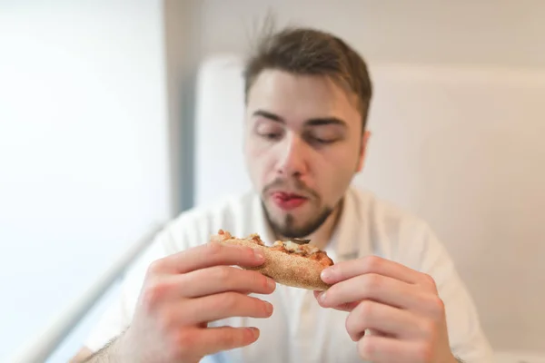 Un hombre hambriento mira de cerca un pedazo de pizza en su mano y está a punto de comerla. . — Foto de Stock