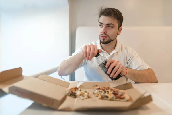 Um homem abre uma garrafa com uma bebida no fundo da pizza. Um homem bebe uma pizza com uma cola. Beber depois de fast food . — Fotografia de Stock