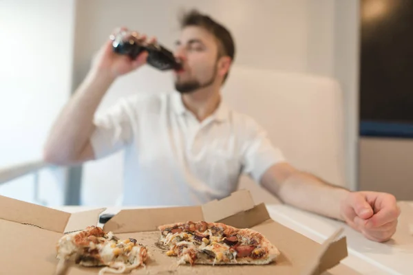 Un hombre bebe una botella después de beber comida rápida. Bebe después de la pizza. Enfoque en pizza . — Foto de Stock