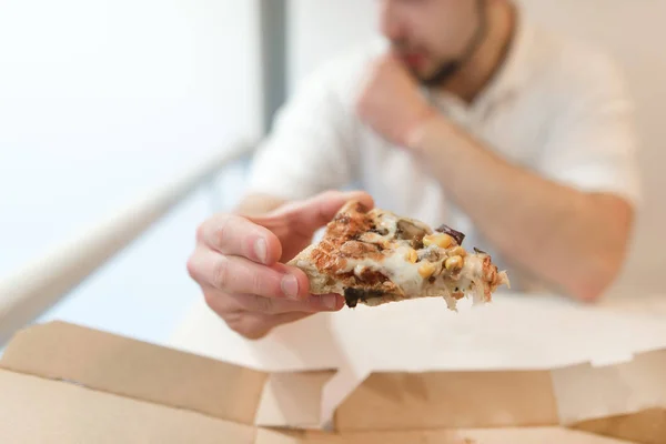 Um homem tem um pedaço de pizza nas mãos. O homem come uma pizza. Concentre-se num pedaço de pizza . — Fotografia de Stock