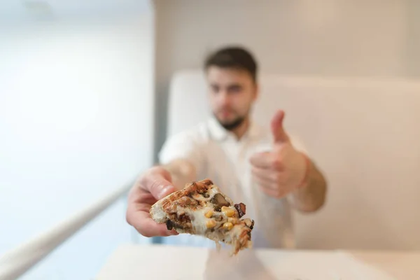 Bir adam bir parça pizza elinde tutar ve onun parmağını girişinde içinde gösterir. Bir adam pizza seviyor. Gibi. — Stok fotoğraf