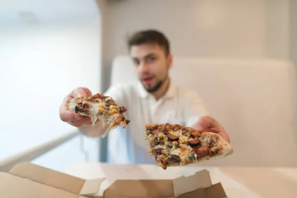 O homem segura duas peças de pizza em suas mãos e as envia para a câmera. Um homem oferece uma pizza. Uma deliciosa pizza nas mãos de um cara . — Fotografia de Stock