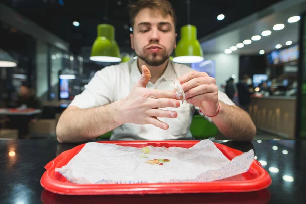 Si pulisce le dita dopo pranzo al fast food. Il ragazzo a tavola e vassoio pulisce le mani dalla salsa . — Foto Stock