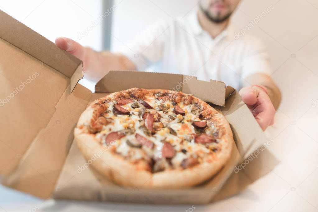 A man holds a box of appetizing pizza in his hands and offers it to others. A man with a fastfood in his hands.