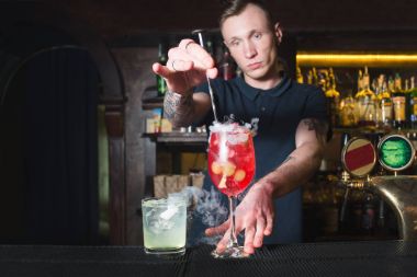 Barmen güzel bir kırmızı kokteyl oluşturur. Barmen alkollü kokteyl maddelerin karışımları.