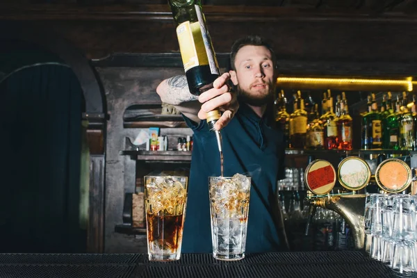 The barman makes an alcoholic cocktail in a nightclub. A man bartender pours alcohol from a bottle into a cocktail.