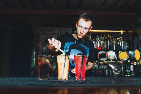 A man bartender creates beautiful alcoholic cocktails. The barman makes cocktails at the bar counter.