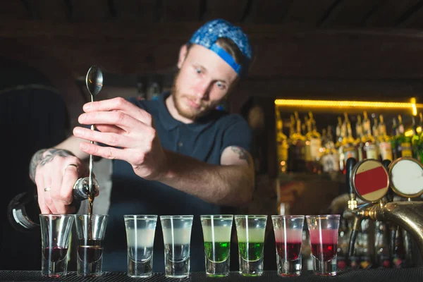 Il barista crea shot alcolici. Il bramen versa l'alcool da una bottiglia in occhiali. Alcol saporito e bello . — Foto Stock