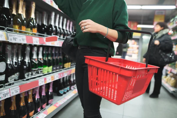 Kırmızı bir alışveriş çantası olan bir kadın, bir süpermarkette alkol seçer. Süpermarket ürün yelpazesi. Depodaki şarap tercih.