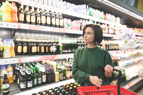 Hermosa chica posando en un supermercado en el fondo de los estantes con productos. El comprador compra los productos en el supermercado — Foto de Stock