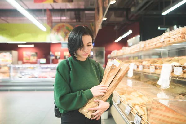 Девушка покупает хлеб в супермаркете. Девушка с хлебными багетами в руках ходит по супермаркету . — стоковое фото