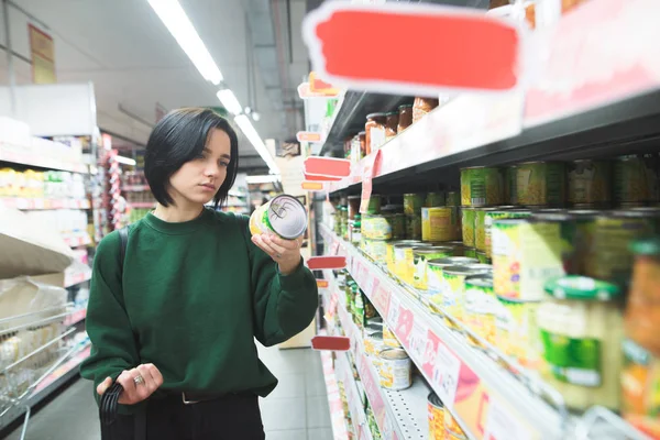 A menina lê o rótulo do produto ao fazer compras em um supermercado. A menina escolhe os bens na loja . — Fotografia de Stock