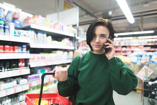 Retrato de una hermosa chica hablando por teléfono mientras compraba en un supermercado. La aventura se rumorea por teléfono en la tienda . — Foto de Stock