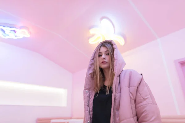 Una hermosa chica con una chaqueta rosa se encuentra en una habitación con el interior de color rosa y mira a la cámara. Linda chica en una habitación rosa . —  Fotos de Stock