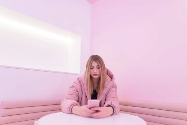 テーブルに座っていると ソフトの部屋でスマート フォンを使用してピンクのドレスの女の子 — ストック写真