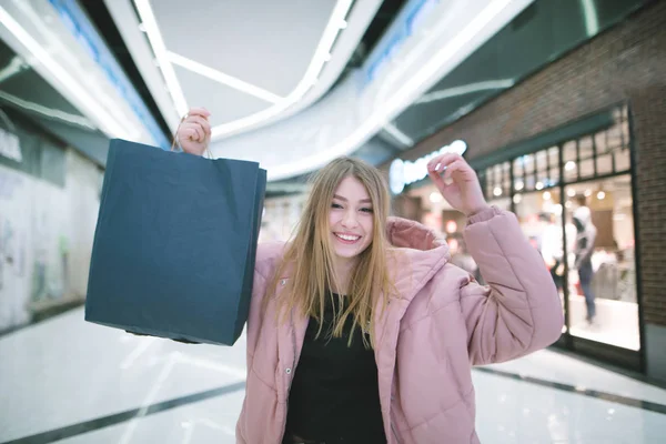 Ein lächelndes blondes Mädchen hob beim Einkaufen im Einkaufszentrum Einkaufstüten in die Höhe. Einkaufskonzept. — Stockfoto