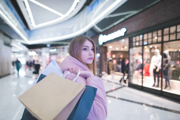 Una rubia dulce con bolsas de compras en el yugo va al centro comercial y mira hacia un lado. Concepto de compras . — Foto de Stock