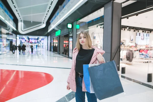 Stilfuld pige med pakker i hænderne står på baggrund af butikker i indkøbscentret. Indkøbskoncept . - Stock-foto