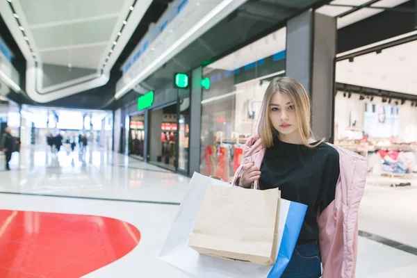 Potret seorang gadis cantik dengan tas belanja di tangannya terhadap pusat perbelanjaan. Konsep Belanja . — Stok Foto