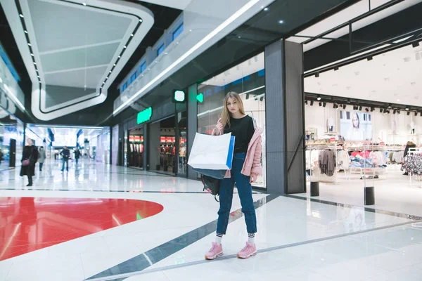 Seorang gadis bergaya dengan tas belanja di tangannya berdiri di mal dan toko pakaian. Konsep Belanja . — Stok Foto