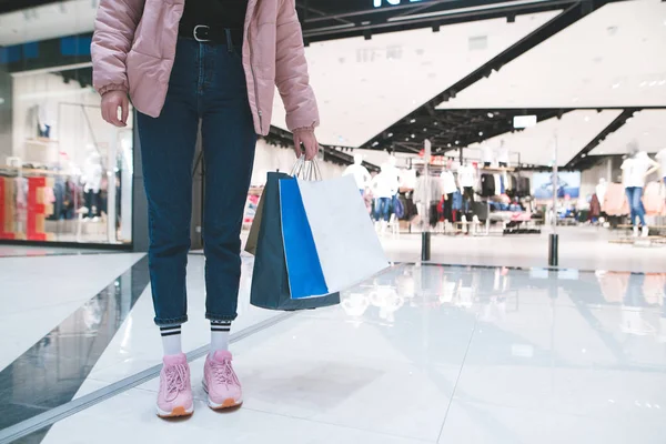 Snygg tjej med shoppingkassar i hennes hand mot bakgrund av en klädaffär i gallerian. Shopping koncept. — Stockfoto