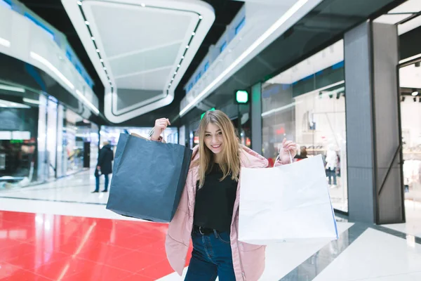 Gadis cantik bersukacita dalam berbelanja. Potret seorang gadis dengan tas belanja di latar belakang pusat perbelanjaan. Konsep Belanja . — Stok Foto