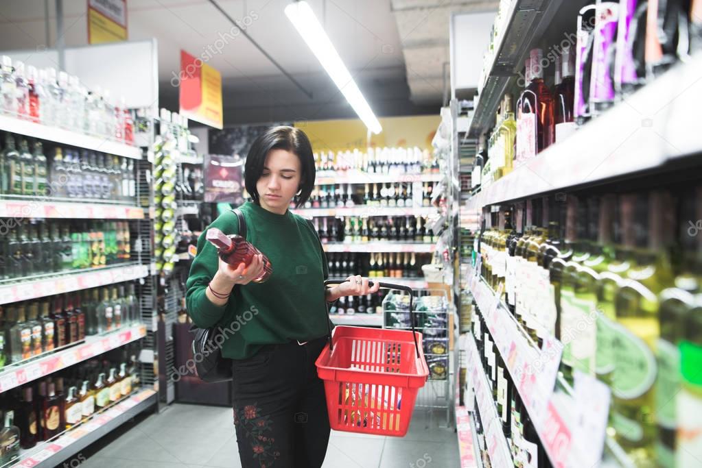 Portrait of a girl who chooses alcohol in a supermarket. Her husband looks at the wine bottle at the time of shopping. Shopping in the supermarket