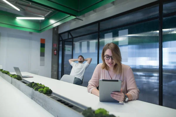 Schöne Mädchen arbeitet in einem Büro auf einem Tablet auf dem Hintergrund ihres Mannes ruht. Büroangestellte im Arbeitsbereich. modernes Büro. — Stockfoto