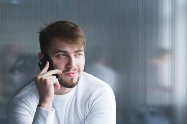 Duvar arka plan üzerinde ofiste telefonla konuşan bir güzel adam beyaz giysili portresi.